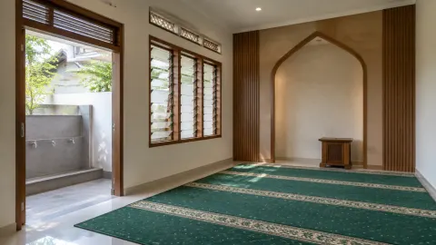 Mushola dengan karpet hijau dan beberapa jendela kayu