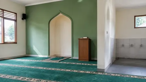 Ruang musala dengan karpet salat dan dinding hijau di depan
