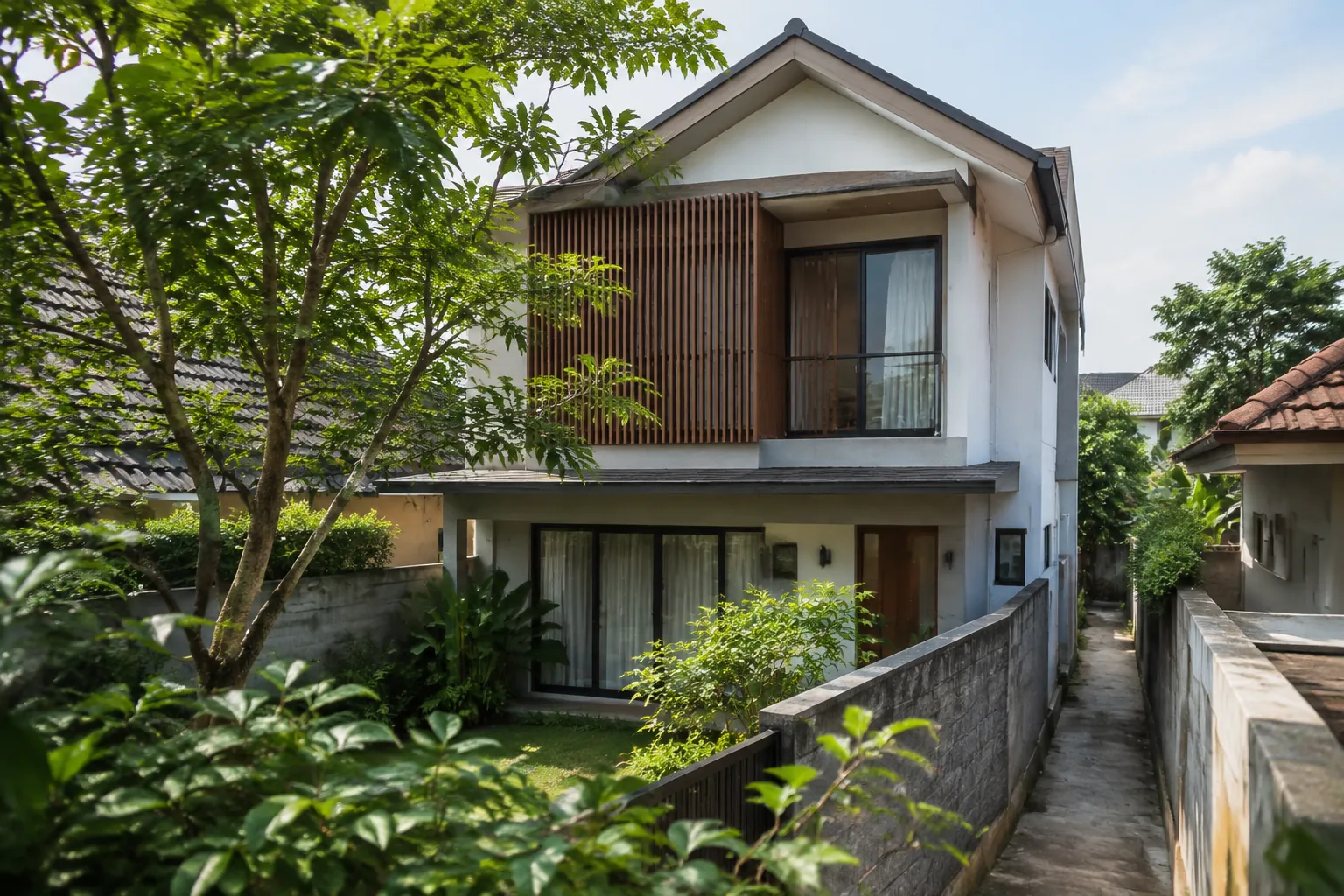 Rumah dua lantai memiliki lorong samping sempit dan tanaman dekat fasad