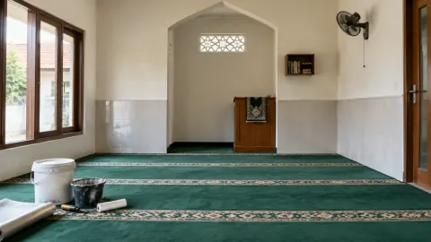 Musala dengan karpet hijau dan perlengkapan kerja di sisi ruang