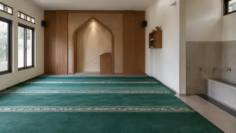 Ruang musala dengan karpet hijau dan ceruk pada dinding kiblat