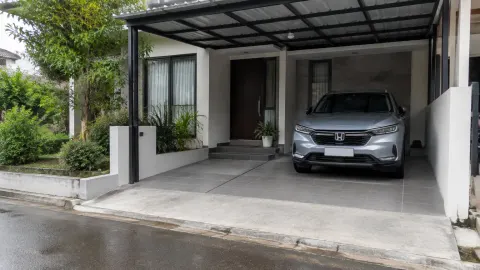 Carport beratap dengan mobil dan lantai keras di depan rumah