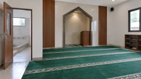 Mushola dengan karpet hijau dan ceruk dinding