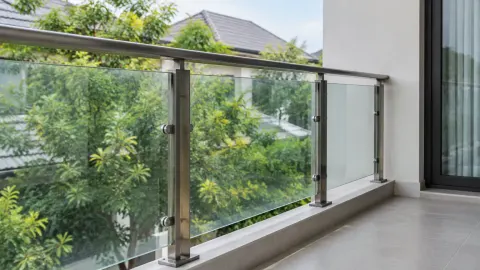 Railing kaca dan logam pada balkon menghadap pepohonan