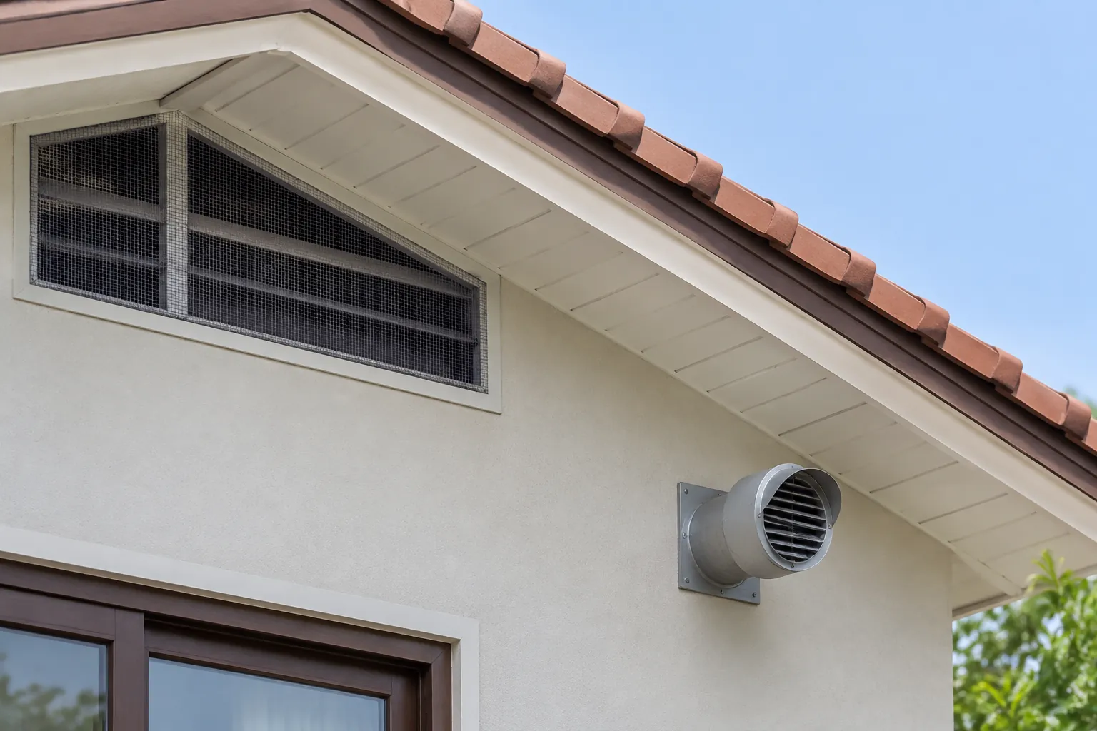 Bukaan ventilasi berjeruji di bawah atap dan outlet bulat terpisah pada dinding luar rumah.