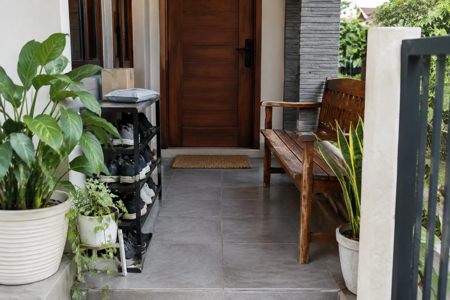 Teras sempit dengan pot tanaman memenuhi sisi jalur menuju pintu