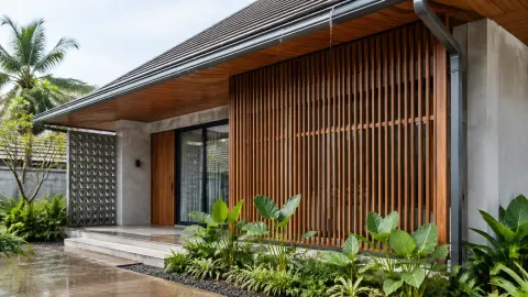 Fasad rumah dengan kisi kayu dan atap menjorok di tengah taman tropis