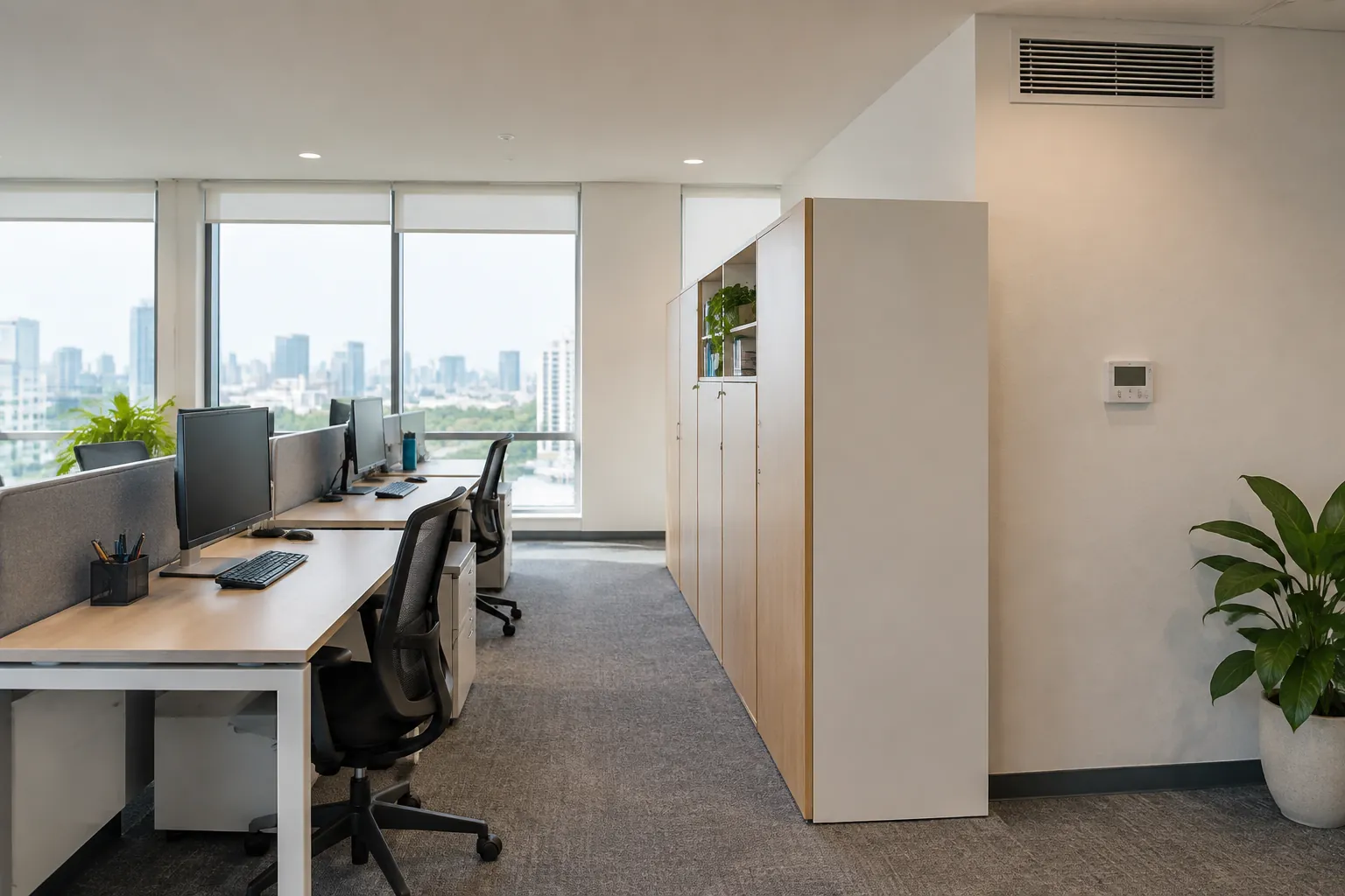 Meja kerja tersusun di dekat jendela dan partisi kantor