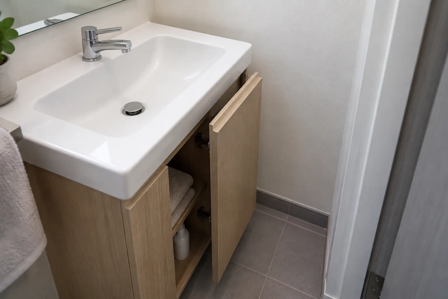 Kabinet bawah wastafel dengan pintu terbuka ke jalur sempit di dekat pintu kamar mandi.