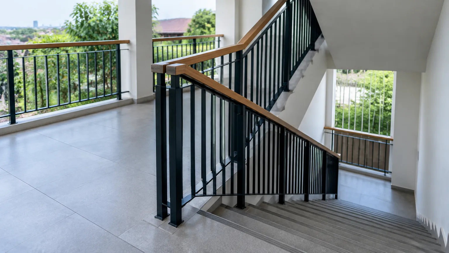 Railing hitam dengan pegangan kayu pada tangga dan balkon