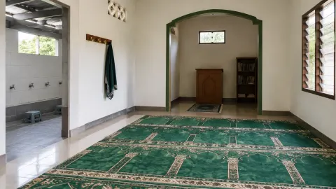 Ruang musala berkarpet dengan area wudu di sisinya