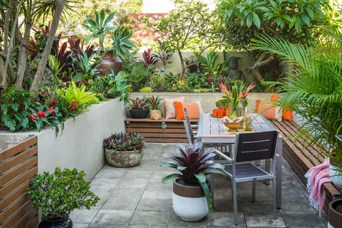 Area duduk taman dengan meja, kursi, bangku, dan tanaman rimbun.
