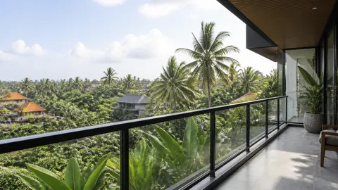 Balkon berpagar kaca dan bingkai gelap menghadap pepohonan tropis