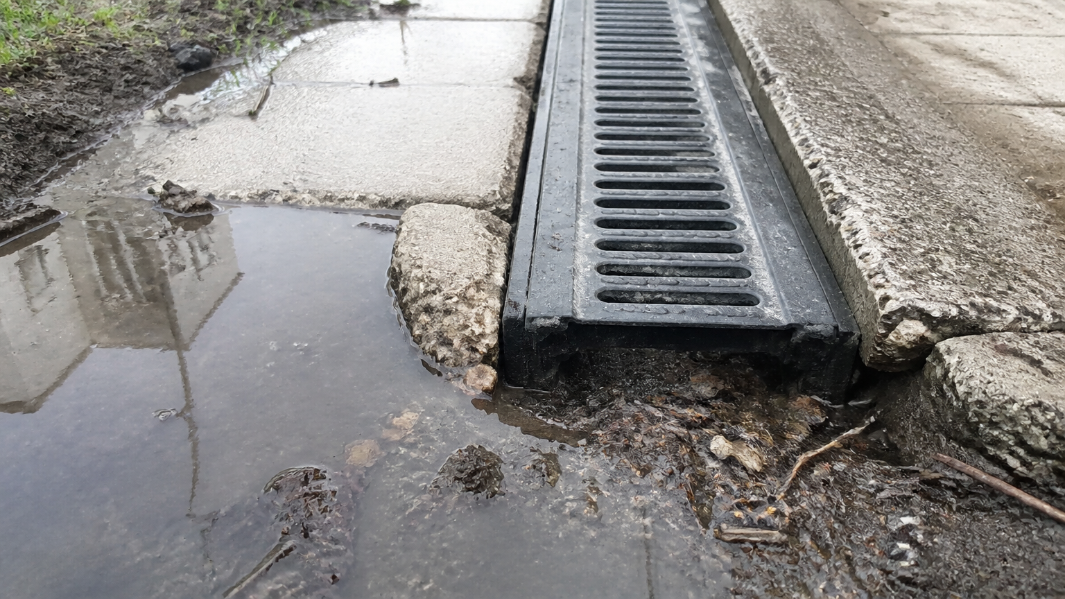 Genangan berlumpur di sekitar saluran berkisi dan permukaan beton retak Genangan berlumpur di sekitar saluran berkisi dan permukaan beton retak
